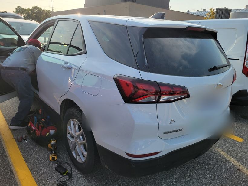 Technician working inside a white fleet SUV with tools staged on the pavement
