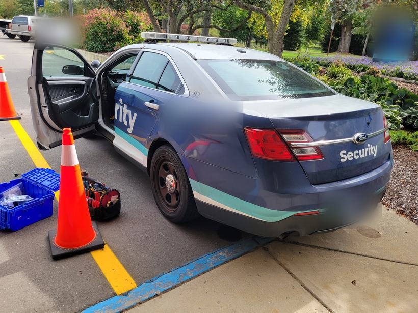 Security patrol sedan with door open and installer tool bag on the pavement